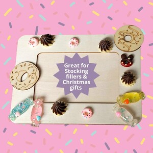 May include: Wooden picture frame with a white background and a variety of colorful decorations, including donuts, candy, and chocolate. The text "Great for Stocking fillers & Christmas gifts" is written in a purple starburst.