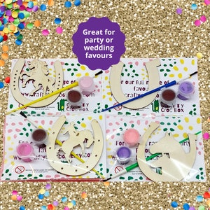 May include: Four wooden horseshoe craft kits with paint pots and brushes. Each horseshoe has a different horse design. The text on the packaging reads "Great for party or wedding favours" and "www.craftycrocbox.com".
