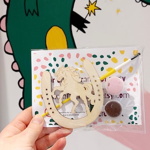 May include: A wooden horseshoe craft kit featuring a unicorn cutout, two pots of paint, a paintbrush, and the text "Craft Party" on the packaging. Suitable for ages 36 months and up due to small parts.