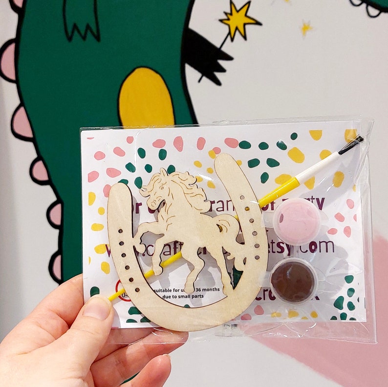 May include: A wooden horseshoe craft kit featuring a unicorn cutout, two pots of paint, a paintbrush, and the text "Craft Party" on the packaging. Suitable for ages 36 months and up due to small parts.