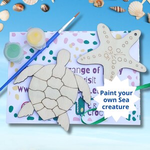 May include: A craft kit with a wooden turtle and starfish, paint pots, and a paintbrush. The kit includes the text "Paint your own Sea creature" on a white background with a blue and green border. Seashells are in the background.