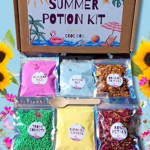 May include: A "SUMMER POTION KIT" craft box containing clear bags of ingredients: pink "Flamingo Fizz", blue "Summer Sky", and orange "Orange Crumble". A wooden spoon and other components are also visible. Measurements are in cm.