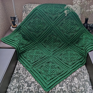 May include: A green crochet blanket with a Celtic knot pattern. The blanket is folded and draped over a chair. The text "CROCHET PATTERN PHOTO TUTORIAL ENGLISH RUSSIAN" is visible in the image.