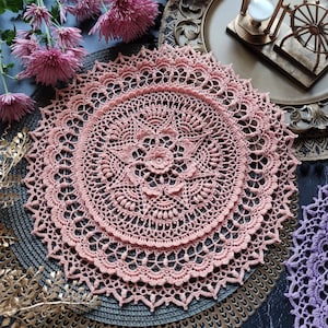 May include: A detailed image of a pink crocheted doily featuring a floral centre and a delicate lace edge. The doily is circular and sits on a dark surface. Text in the image reads "CROCHET PATTERN PHOTO TUTORIAL" and "ENGLISH RUSSIAN".