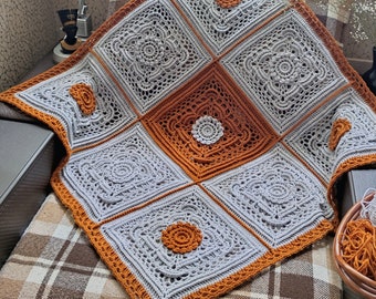 May include: A crochet blanket made of square motifs in light gray and burnt orange yarn. The text on the left reads: CROCHET PATTERN PHOTO TUTORIAL, ENGLISH RUSSIAN. The blanket features intricate circular and geometric stitch patterns.