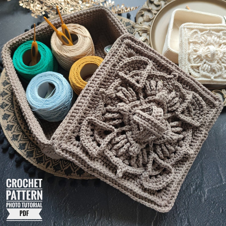 May include: A crocheted square box with a brown lid and a detailed floral pattern. The box is open and filled with colorful yarn balls and crochet hooks.