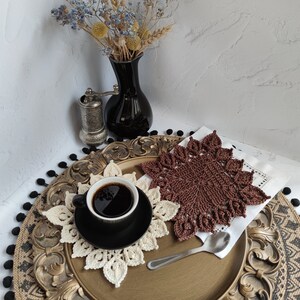 K&ouml;nnte beinhalten: Eine braune H&auml;keldeckchen mit einem wei&szlig;en H&auml;keldeckchen darauf. Eine Tasse Kaffee steht auf dem wei&szlig;en H&auml;keldeckchen. Die Deckchen befinden sich auf einem goldenen Tablett mit schwarzem Hintergrund.