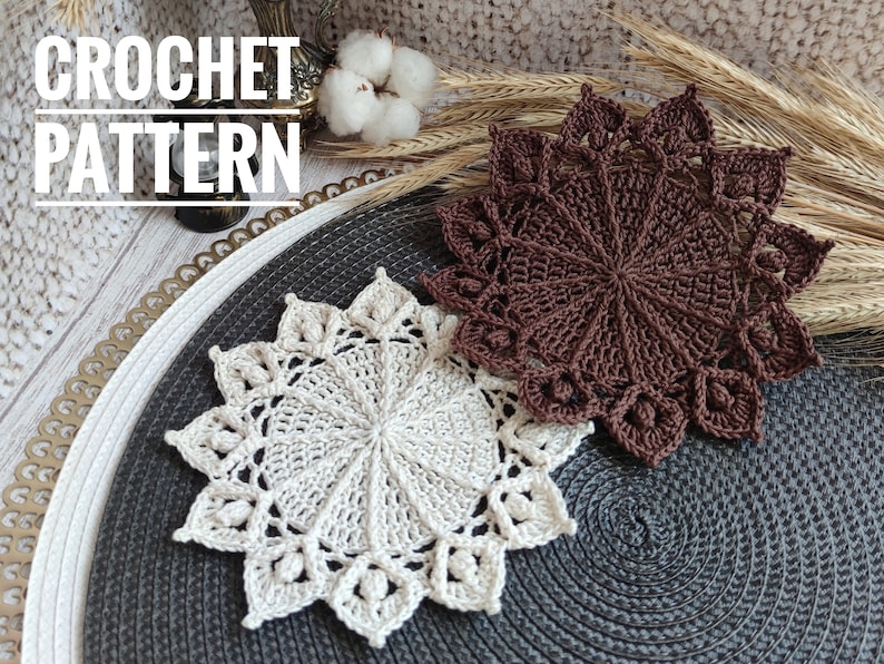 May include: Two crocheted doilies, one in brown and one in cream, on a grey and white round placemat. The text "CROCHET PATTERN" is visible at the top of the image.