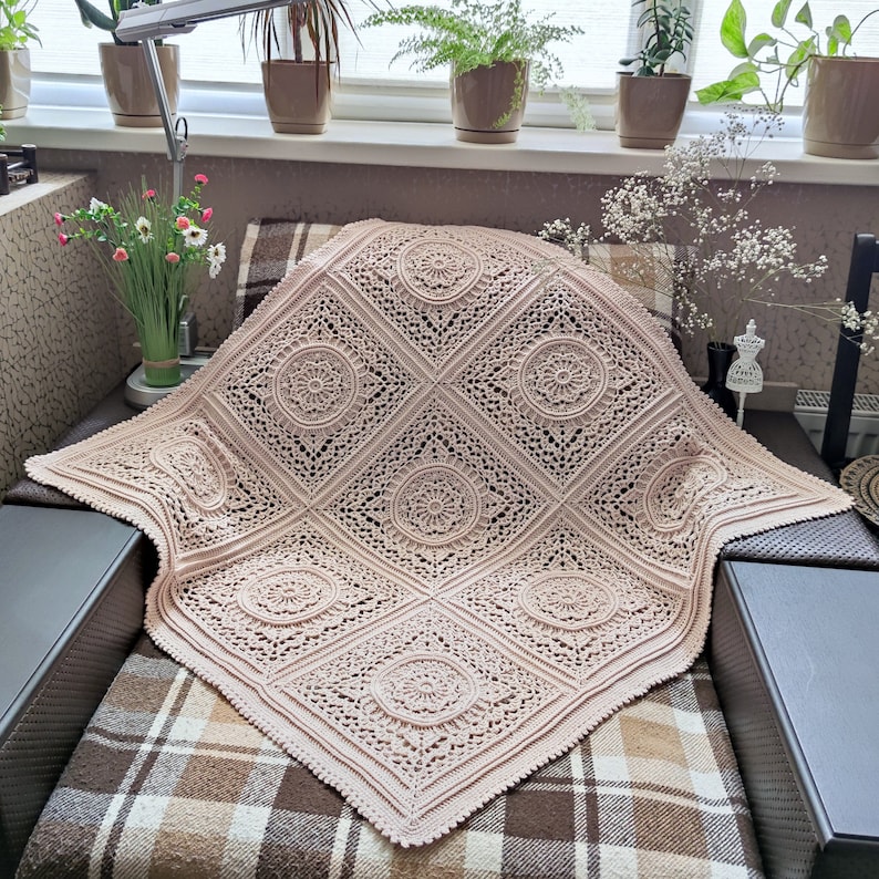 Pu&ograve; includere: Una coperta all'uncinetto di colore rosa chiaro con un motivo delicato e intricato. La coperta &egrave; composta da quadrati ripetuti con un disegno circolare al centro di ogni quadrato.