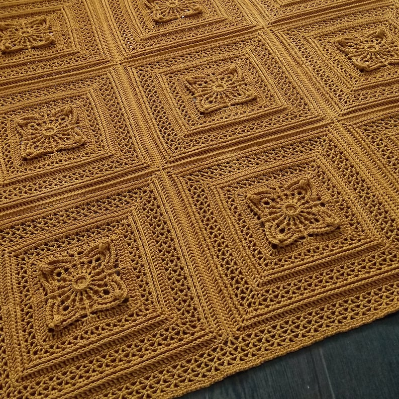 May include: A mustard yellow crochet blanket featuring a repeating pattern of square motifs. Each square consists of a central floral-like design surrounded by concentric geometric borders with intricate openwork stitching throughout.