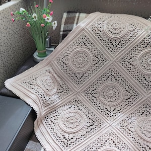 Pu&ograve; includere: Una coperta all'uncinetto di colore beige chiaro con un delicato e intricato motivo di cerchi e quadrati.