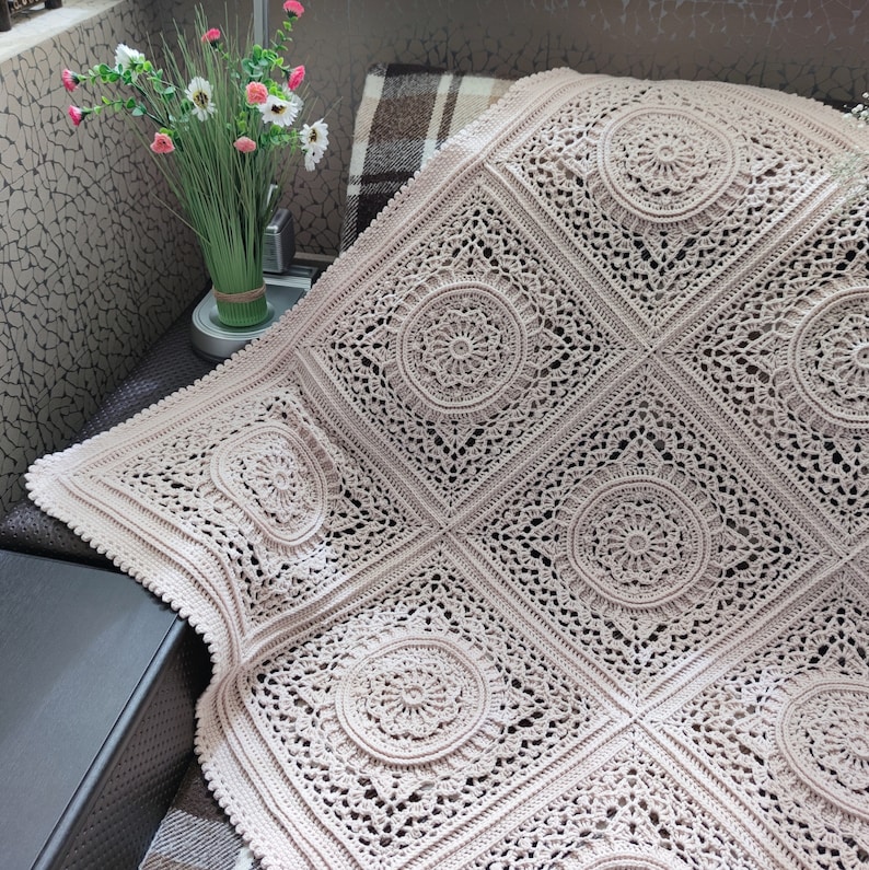 Pu&ograve; includere: Una coperta all'uncinetto di colore beige chiaro con un delicato e intricato motivo di cerchi e quadrati.