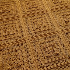 May include: Mustard yellow crocheted blanket with a repeating square pattern. Each square features a raised floral design in the center, surrounded by intricate openwork. The blanket is made of a soft, textured yarn.