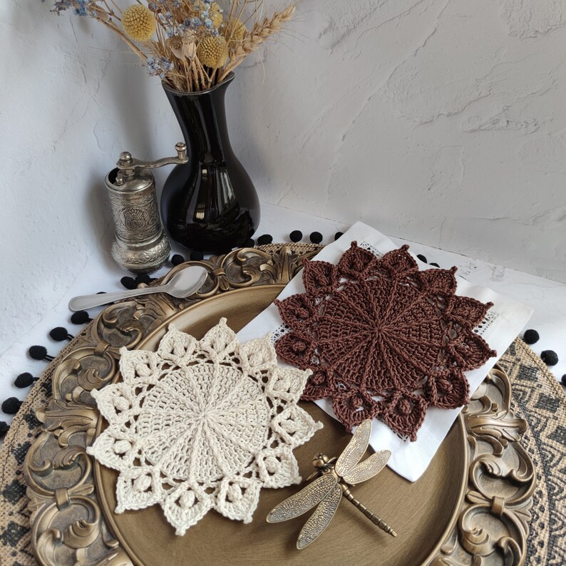 May include: Two crocheted doilies, one brown and one white, on a gold and black decorative tray. The tray has a white surface with a brown doily on top. The white doily is on the bottom of the tray.