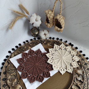 May include: Two crocheted doilies, one brown and one white, on a gold and black decorative tray. The doilies are circular and have a delicate lace pattern.