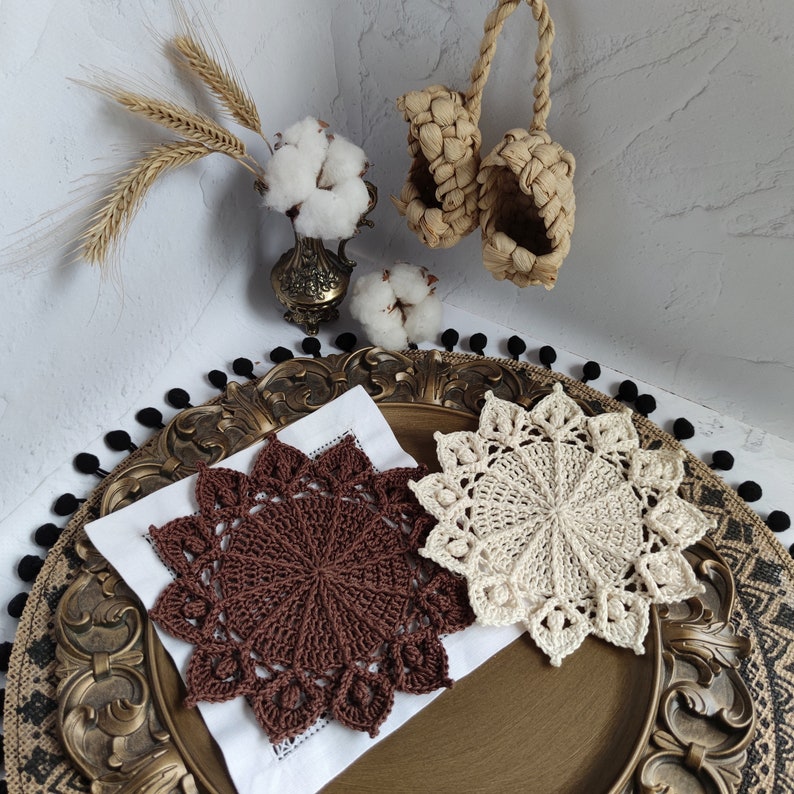 May include: Two crocheted doilies, one brown and one white, on a gold and black decorative tray. The doilies are circular and have a delicate lace pattern.