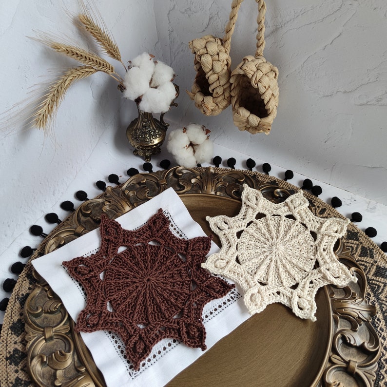 Puede incluir: Dos manteles individuales de ganchillo en forma de estrella, uno marr&oacute;n y otro blanco, se muestran en una bandeja decorativa con acabado dorado. La bandeja tiene un borde de cuentas y est&aacute; hecha de metal.