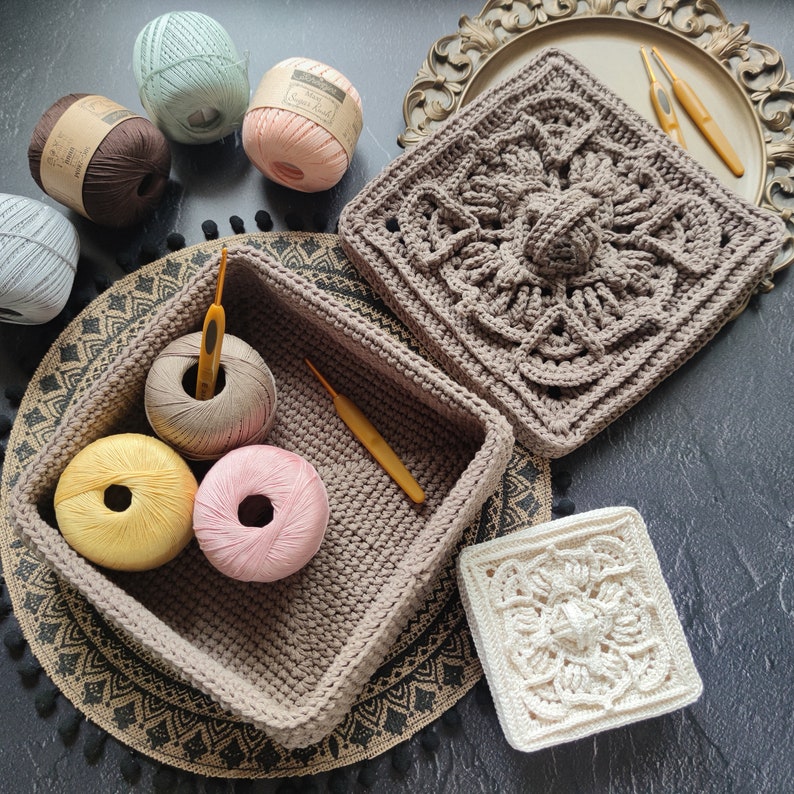 May include: A brown crocheted storage basket with a beige crocheted lid. The basket is filled with yarn balls and crochet hooks. The basket is sitting on a brown and black rug.