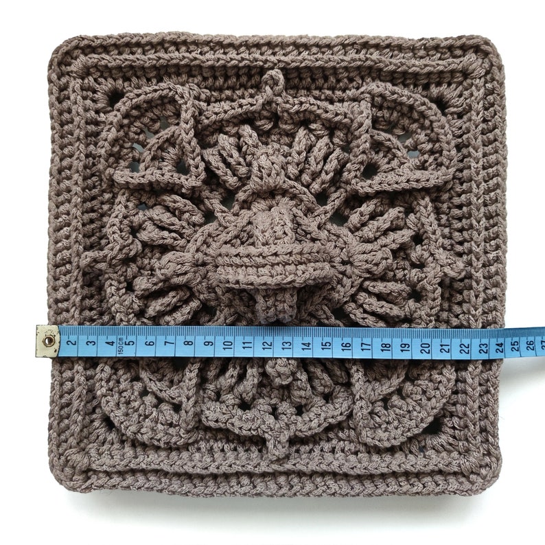 May include: A brown crocheted square measuring 26 inches across. The square has a detailed, intricate design with a central motif.