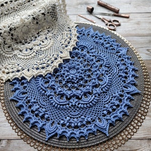 May include: Two crocheted doilies, one white and one blue, are displayed on a round, gold-trimmed, woven placemat. The blue doily is larger and has a more intricate design.