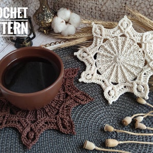 Puede incluir: Dos posavasos de ganchillo en forma de estrella, uno marr&oacute;n y otro beige, sobre una superficie gris texturizada. El posavasos marr&oacute;n est&aacute; debajo de una taza de cer&aacute;mica marr&oacute;n llena de caf&eacute;. El texto "CROCHET PATTERN" es visible en la esquina superior izquierda de la imagen.