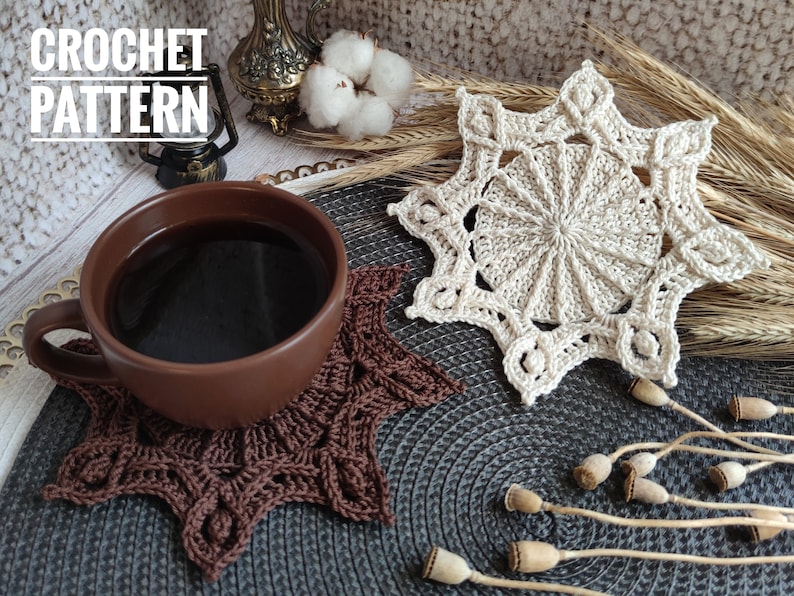 Puede incluir: Dos posavasos de ganchillo en forma de estrella, uno marr&oacute;n y otro beige, sobre una superficie gris texturizada. El posavasos marr&oacute;n est&aacute; debajo de una taza de cer&aacute;mica marr&oacute;n llena de caf&eacute;. El texto "CROCHET PATTERN" es visible en la esquina superior izquierda de la imagen.