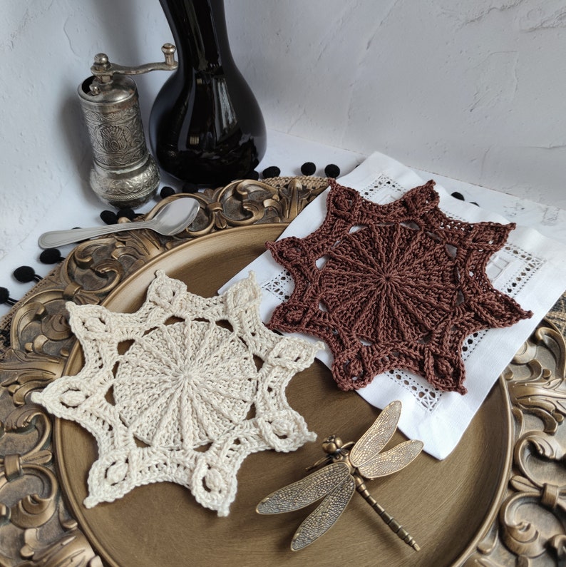 Puede incluir: Dos doilies de ganchillo en forma de estrella, uno marr&oacute;n y otro crema, sobre un plato decorativo con un adorno de lib&eacute;lula.