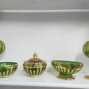 Puede incluir: Conjunto de cuatro cuencos y jarrones de vidrio verde y dorado con intrincados patrones. Los cuencos y jarrones est&aacute;n decorados con un patr&oacute;n repetitivo de hojas doradas sobre un fondo verde.