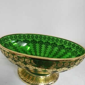 Puede incluir: Un taz&oacute;n grande de vidrio verde de forma ovalada con bordes dorados y un patr&oacute;n floral decorativo. El taz&oacute;n se asienta sobre un pedestal dorado.