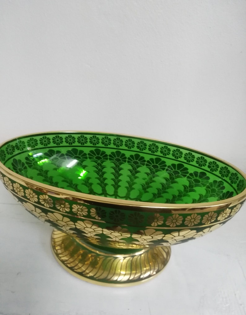 Puede incluir: Un taz&oacute;n grande de vidrio verde de forma ovalada con bordes dorados y un patr&oacute;n floral decorativo. El taz&oacute;n se asienta sobre un pedestal dorado.