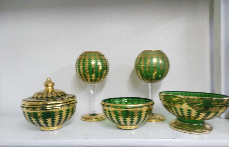 Puede incluir: Conjunto de cinco cuencos y copas de vidrio verde y dorado con un patr&oacute;n decorativo. Los cuencos y las copas son todos del mismo estilo, con una base verde y detalles dorados.