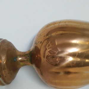 Op de afbeelding: Een koperkleurige vaas in vintage-stijl met een bolvormige body en een uitlopende basis. De vaas heeft een lange, slanke hals en een brede, afgeronde rand. Het koper heeft een warme, reflecterende glans, met tekenen van ouderdom.