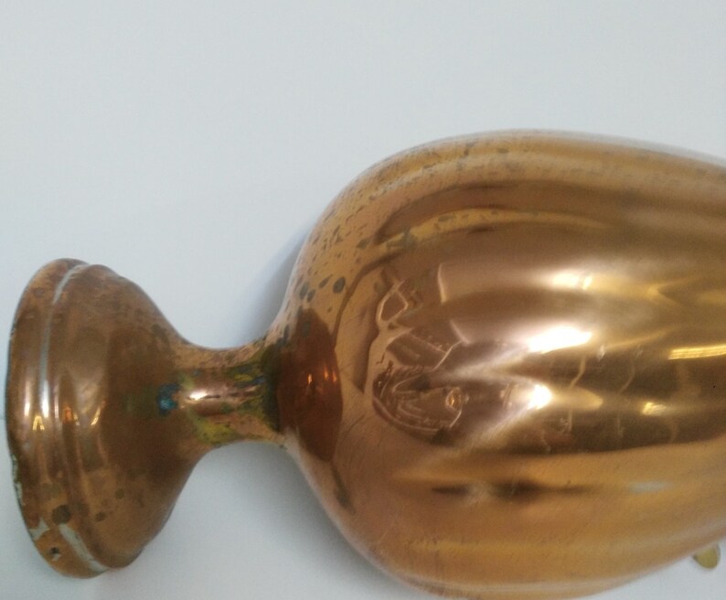 Op de afbeelding: Een koperkleurige vaas in vintage-stijl met een bolvormige body en een uitlopende basis. De vaas heeft een lange, slanke hals en een brede, afgeronde rand. Het koper heeft een warme, reflecterende glans, met tekenen van ouderdom.