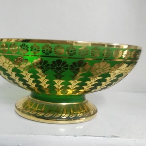 Puede incluir: Un cuenco de vidrio verde con detalles en pan de oro. El cuenco tiene una base ancha y redondeada y un borde acampanado. El dise&ntilde;o en pan de oro presenta motivos florales y geom&eacute;tricos.