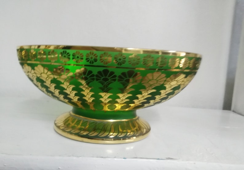 Puede incluir: Un cuenco de vidrio verde con detalles en pan de oro. El cuenco tiene una base ancha y redondeada y un borde acampanado. El dise&ntilde;o en pan de oro presenta motivos florales y geom&eacute;tricos.