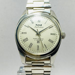 May include: A silver HMT Jubilee wristwatch with a white face and Roman numeral hour markers. The watch has a silver metal band and says "Para Shock 17 Jewels" on the face.