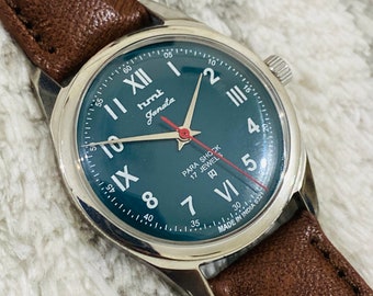 May include: A silver wristwatch with a dark blue face and white Roman numeral hour markers. The watch has a brown leather band and says "hmt Janata" and "Para Shock 17 Jewels" on the face.