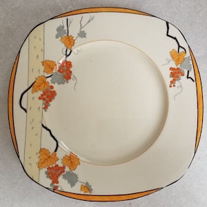 Puede incluir: Plato cuadrado color crema con ribete naranja y negro. El plato está decorado con un diseño de vid con hojas naranjas y uvas rojas. Una pieza decorativa para servir comida.