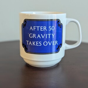 May include: White ceramic mug with a blue and black graphic that says "After 50 Gravity Takes Over".