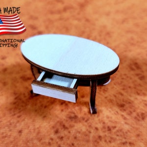 May include: A small, white oval table with a drawer. The table is made of wood and has a simple design. It is sitting on a brown surface.