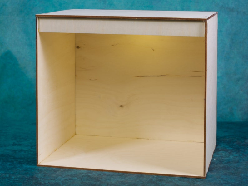 May include: A plain, light wood, empty display box with a light inside. The box is made of plywood and has a simple, rectangular shape.