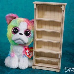 Pu&ograve; includere: Una libreria in legno con cinque ripiani. La libreria &egrave; bianca e ha un design semplice. "STUFFED TOY NOT INCLUDED" &egrave; scritto nella parte inferiore dell'immagine.