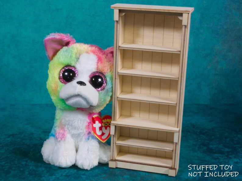 Pu&ograve; includere: Una libreria in legno con cinque ripiani. La libreria &egrave; bianca e ha un design semplice. "STUFFED TOY NOT INCLUDED" &egrave; scritto nella parte inferiore dell'immagine.