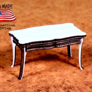 May include: A white wooden table with a black trim and four legs. The table is made of wood and has a simple design. The table is on a brown surface.