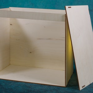 May include: A wooden photography box with a removable back panel. The box is made of light wood and has a simple design.