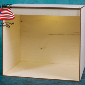May include: A plain, unfinished wooden box with a light brown color. The box is empty and has a rectangular shape. The box is made of plywood and has a smooth surface.