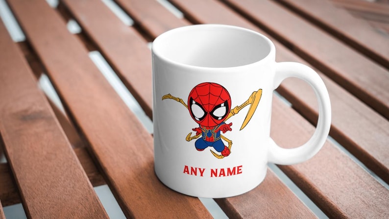 Puede incluir: Taza de cer&aacute;mica blanca con una imagen de dibujos animados de Spider-Man con un traje rojo y azul con detalles dorados. La taza tiene un asa y el texto "ANY NAME" impreso en la parte inferior.
