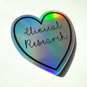 May include: A holographic heart-shaped sticker with a black outline and the text "clinical research" in black.