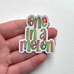 May include: A white sticker with the text "one in a melon" in green and red lettering with black speckles.