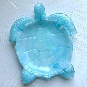 May include: A light blue decorative turtle-shaped dish. The dish has a glossy finish and a textured surface, with a design that mimics a turtle's shell. The dish is a decorative item.